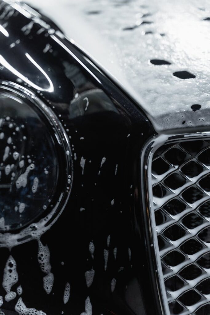 Detailed view of a luxury black car covered with soap suds during a wash.