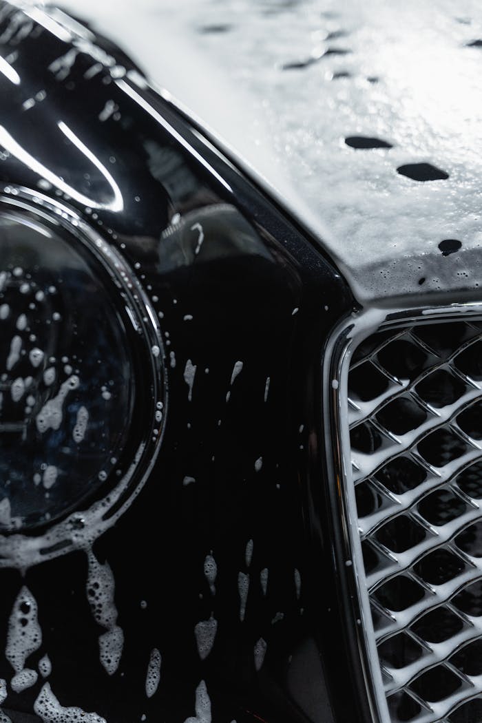 Detailed view of a luxury black car covered with soap suds during a wash.